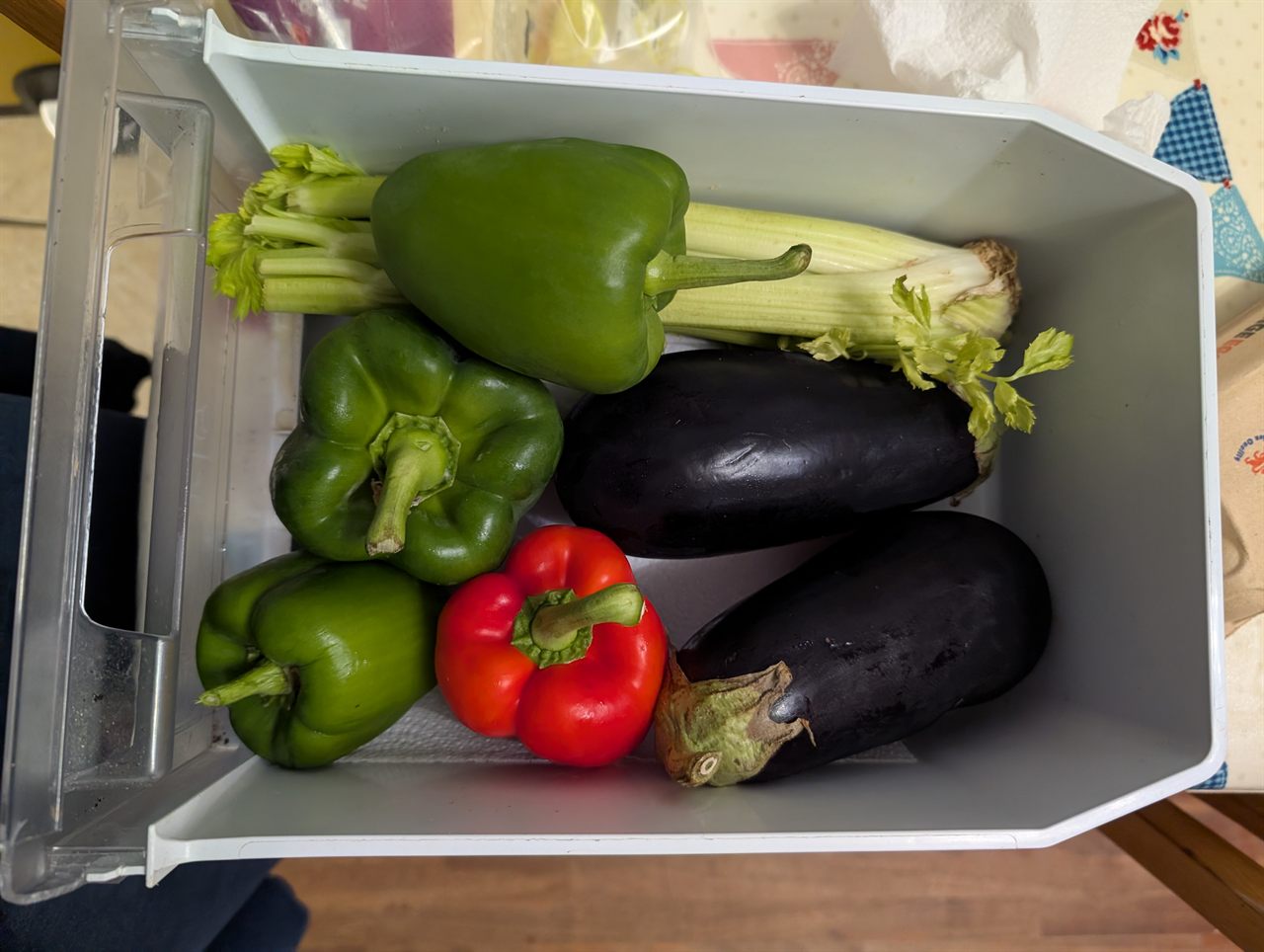 A vegetable drawer with aubergines, peppers and celery